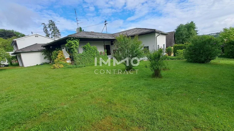 Einfamilienhaus mit großem Garten und grüner Fassadenbegrünung unter bewölktem Himmel.