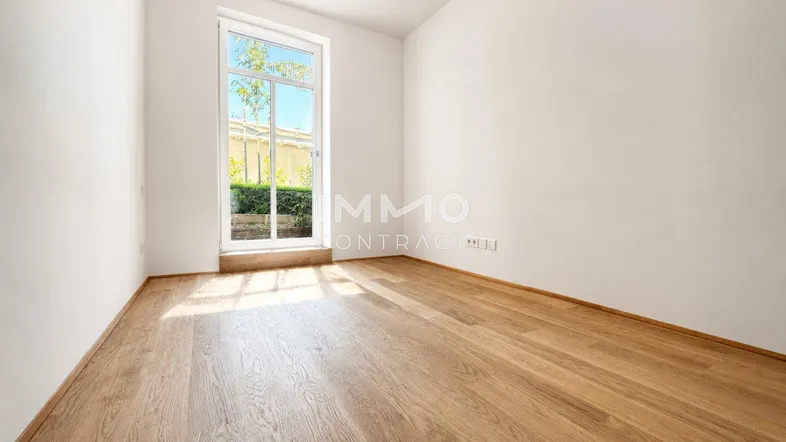 Heller, leerer Raum mit weißen Wänden und Holzboden, bietet Zugang zum Außenbereich.
