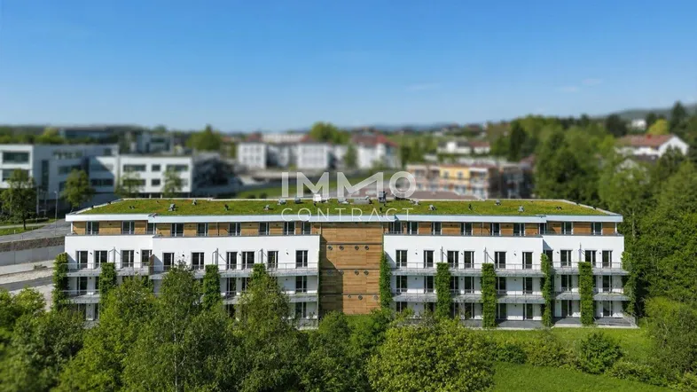 Modernes Mehrfamilienhaus mit begrüntem Flachdach und Balkonen, umgeben von viel Grün.
