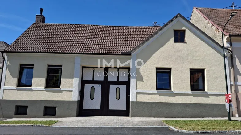 Traditionelles Einfamilienhaus mit heller Fassade und braunem Dach unter blauem Himmel.