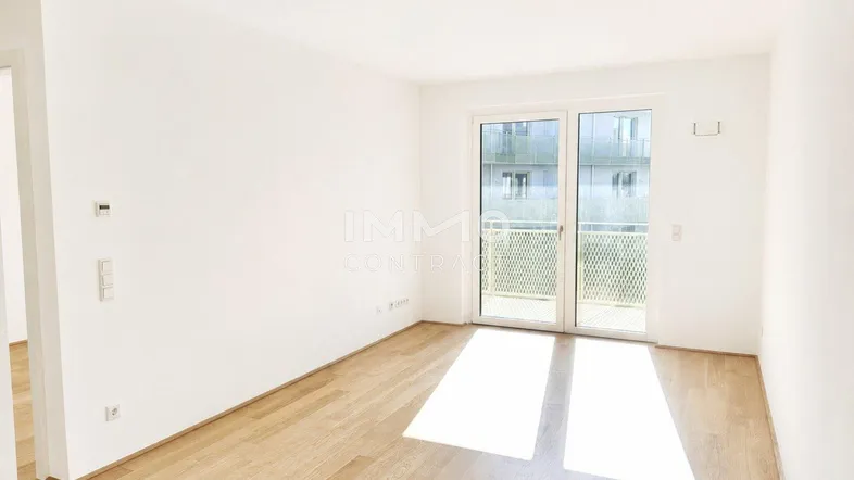 Helles, leeres Zimmer mit Parkettboden und Zugang zu einem Balkon, ideal als Wohnbereich.