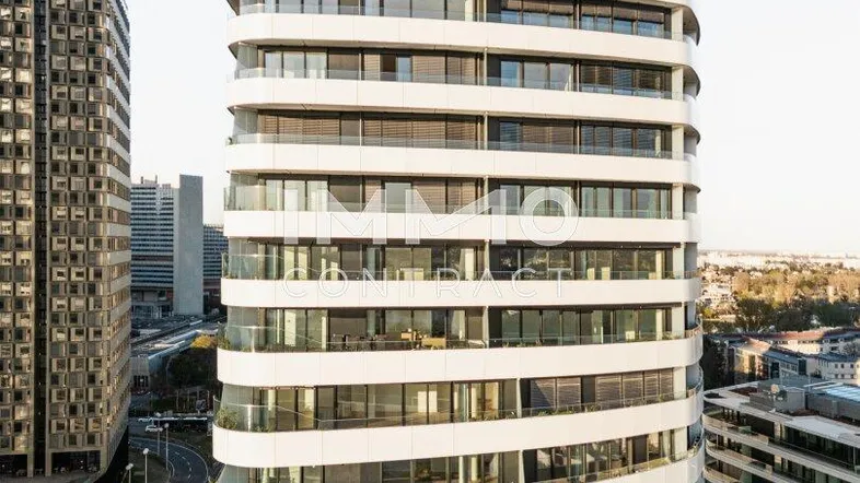 Moderne Hochhausfassade mit geschwungenen Balkonen und großen Fenstern in urbaner Umgebung.