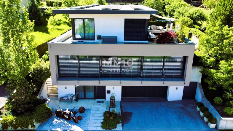 Moderne Villa mit Flachdach, großer Dachterrasse und integrierter Garage, umgeben von viel Grün.
