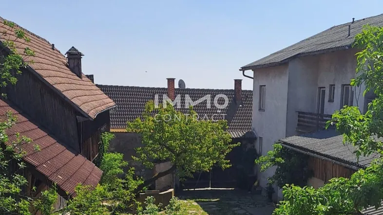 Innenhof mit altem Baumbestand und mehreren Gebäuden unter blauem Himmel.