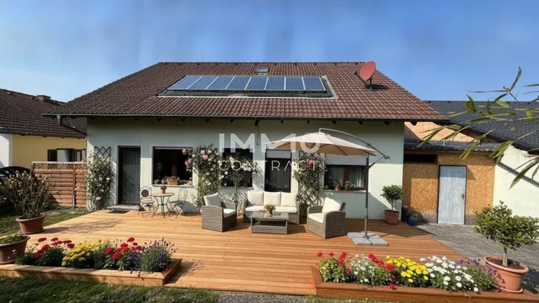 Große Holzterrasse mit Gartenmöbeln und bunten Blumenbeeten vor dem Haus mit Solaranlage.