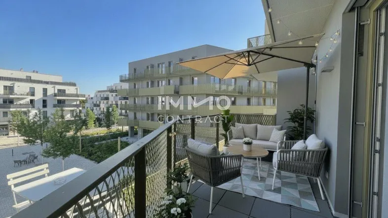 Möblierter Balkon mit Sitzgelegenheiten, Sonnenschirm und Blick auf moderne Wohngebäude.