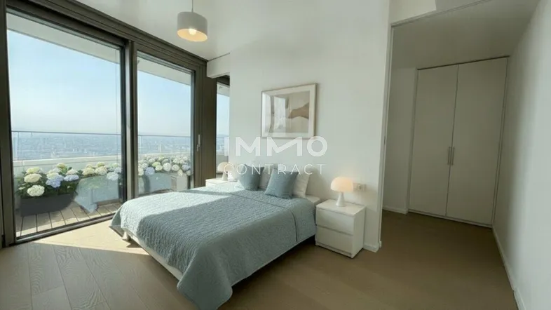 Helles Schlafzimmer mit Holzboden, großen Fenstern und Zugang zum Balkon mit Stadtblick.