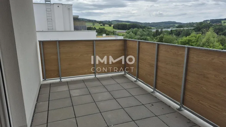 Geräumiger Balkon mit Fliesenboden und Holzverkleidung, bietet einen weiten Blick ins Grüne.