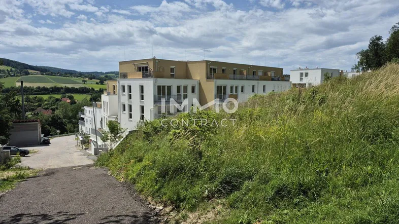 Modernes Gebäude auf einem Hügel mit weitem Blick über die grüne Landschaft unter bewölktem Himmel.