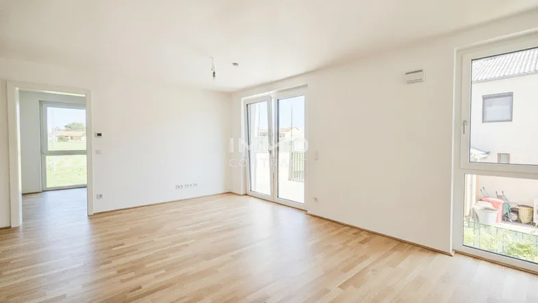 Heller, leerer Wohnraum mit hellem Holzplankenboden und Zugang zu einem Balkon oder einer Terrasse.