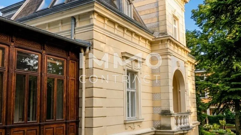 Historische Villa mit Mansarddach und dekorativen Elementen, umgeben von einem gepflegten Garten.