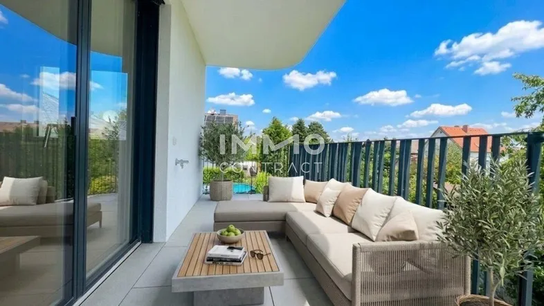 Möblierter Balkon mit bequemen Outdoor-Sofa, Kaffeetisch und weitem Blick ins Grüne unter blauem Himmel.