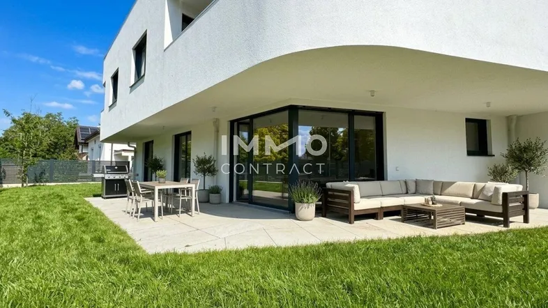 Moderne Terrasse mit Sitzgelegenheiten und Grillbereich, umgeben von einer gepflegten Rasenfläche.