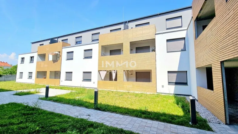 Moderne Wohnanlage mit weißer und holzverkleideter Fassade sowie kleinen Grünflächen davor.