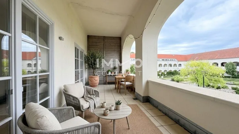Möblierter Balkon mit Rundbögen und Blick auf einen gepflegten Innenhofgarten.