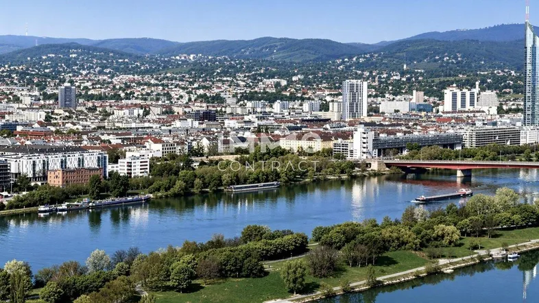 Panoramablick über die Stadt mit Fluss, Brücken und Bergen im Hintergrund unter blauem Himmel.
