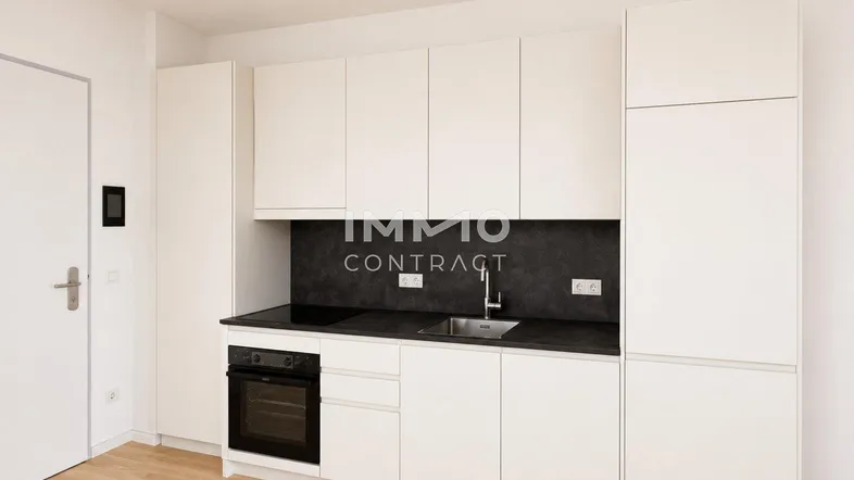 Moderne, kompakte Küche mit weißen Schränken, dunkler Arbeitsplatte und integriertem Backofen.