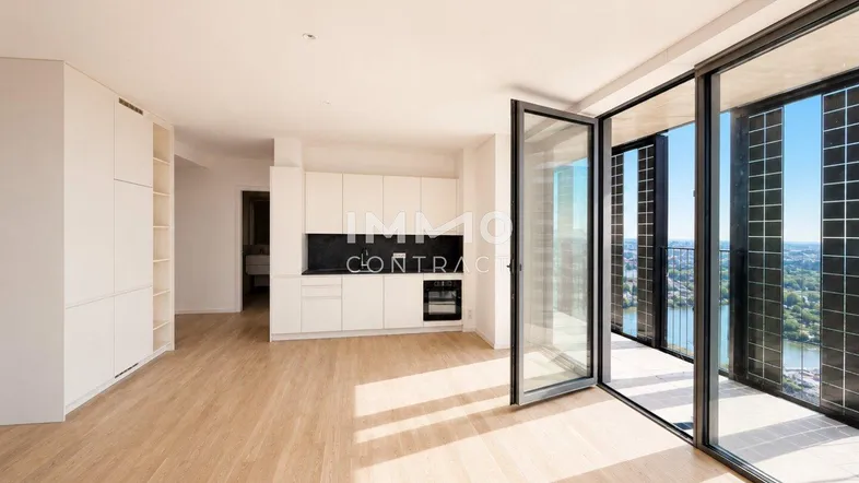 Helles, offenes Wohnzimmer mit integrierter Küche, Holzboden und großen Glasfronten mit Flussblick.