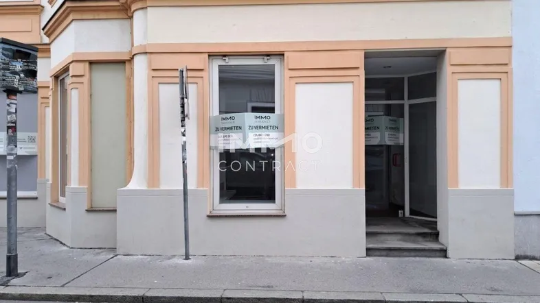 Straßenansicht eines Geschäftsgebäudes mit Eingang und Schaufenstern im Erdgeschoss.