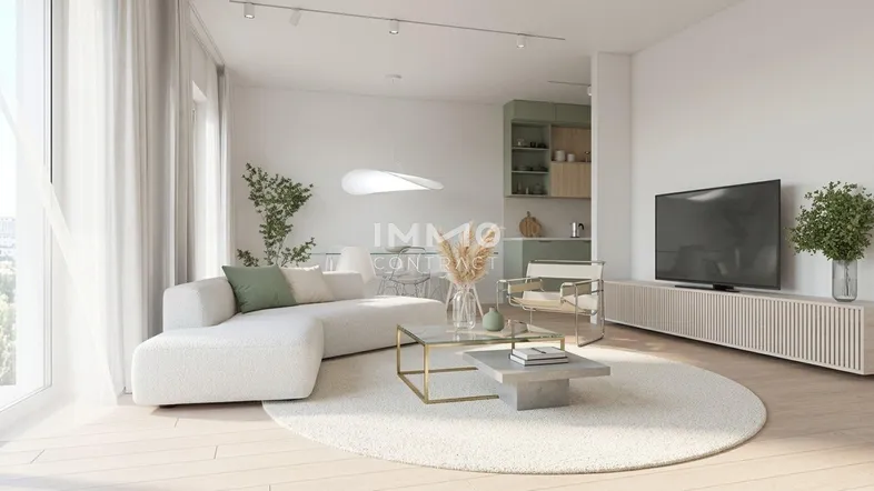 Heller offener Wohnbereich mit modernem Sofa, Fernseher und Blick auf eine integrierte Küchenzeile.
