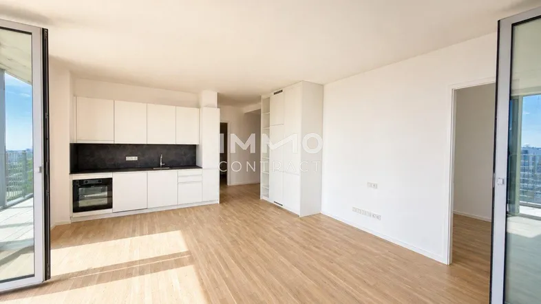 Heller offener Wohnbereich mit integrierter Küche, Holzboden und Zugang zu einem Balkon.