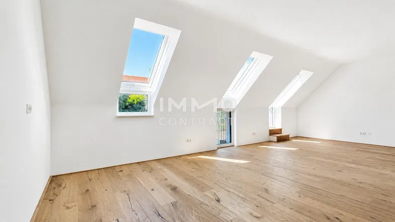 Heller Dachgeschossraum mit schrägen Wänden, Holzboden und mehreren Dachfenstern für viel Tageslicht.