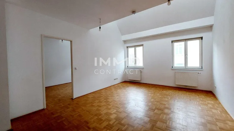 Geräumiges Wohnzimmer mit Parkettboden, zwei Fenstern und schrägen Decken.