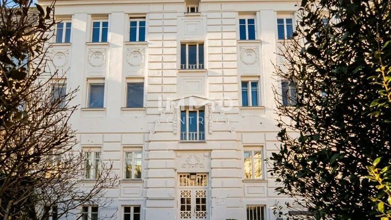 Elegante weiße Fassade eines klassischen Gebäudes mit vielen Fenstern und gepflegter Umgebung.