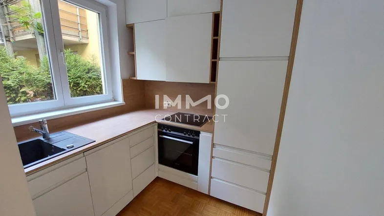 Moderne kleine Küche mit weißen Schränken, Holztheke, integriertem Ofen und Blick ins Grüne.