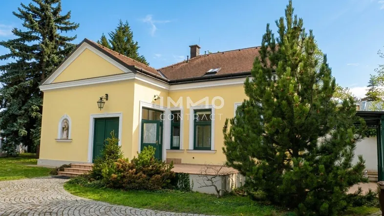 Gelbes Haus mit grünen Fensterläden und Türen, umgeben von Bäumen und einem gepflasterten Weg.