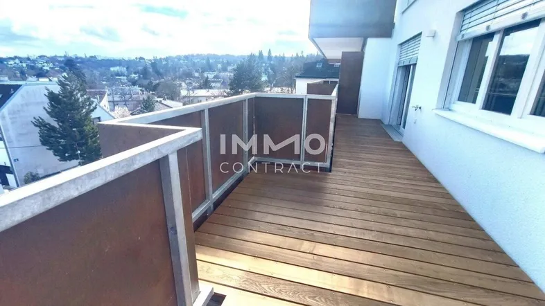 Geräumiger Balkon mit Holzboden und Blick auf die umliegende Wohngegend und Bäume.