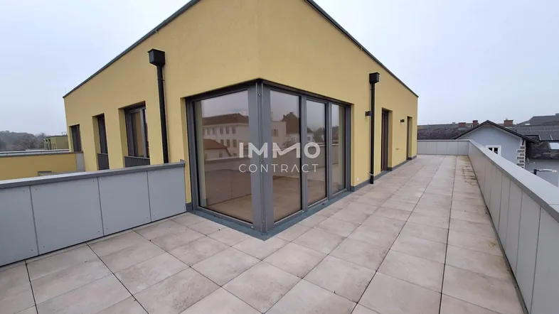 Geräumige Dachterrasse mit Fliesenboden und Zugang zu modernen Wohnräumen in gelbem Gebäude.