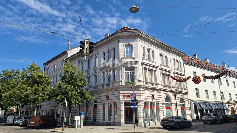 Historisches Eckgebäude in städtischer Umgebung mit Geschäften im Erdgeschoss und Wohnungen darüber.