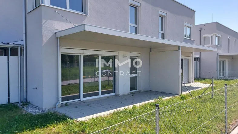 Moderne Reihenhausfassade mit kleiner gepflasterter Terrasse und Zugang zum Gartenbereich.