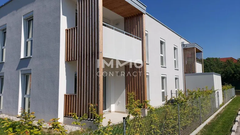 Modernes Mehrfamilienhaus mit weißer Fassade, Holzelementen und Balkonen unter blauem Himmel.