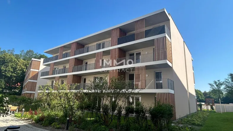 Modernes Mehrfamilienhaus mit mehreren Balkonen und Holzverkleidung unter blauem Himmel.