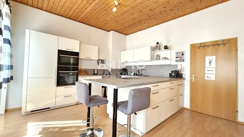Moderne Küche mit weißen Hochglanzfronten, Kochinsel und Holzbalkendecke, gut ausgestattet und hell.
