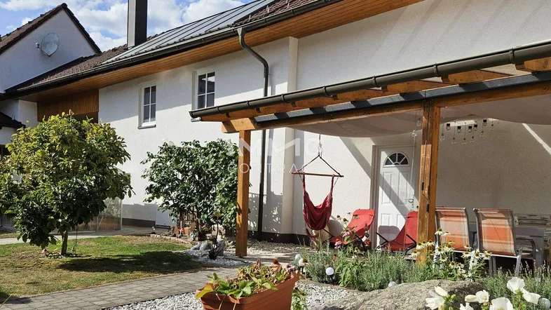 Helles Einfamilienhaus mit überdachter Terrasse, gepflegtem Garten und Photovoltaikanlage auf dem Dach.