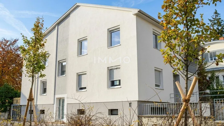 Modernes Mehrfamilienhaus mit heller Fassade und großen Fenstern, umgeben von jungen Bäumen.