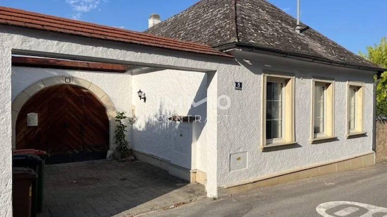 Weiß verputztes Haus mit traditionellem Holztor und schmalen Fenstern an einer ruhigen Straße.