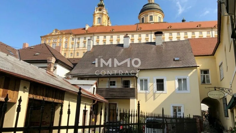 Historisches Gebäudeensemble mit gelbem Haus und imposantem Kloster im Hintergrund.