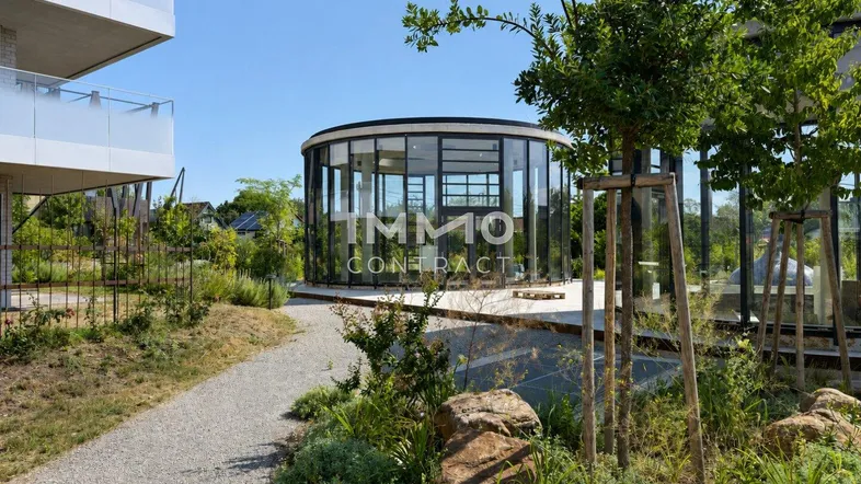 Moderne Architektur mit Glasfassade und begrünten Balkonen in einer gepflegten Gartenanlage.