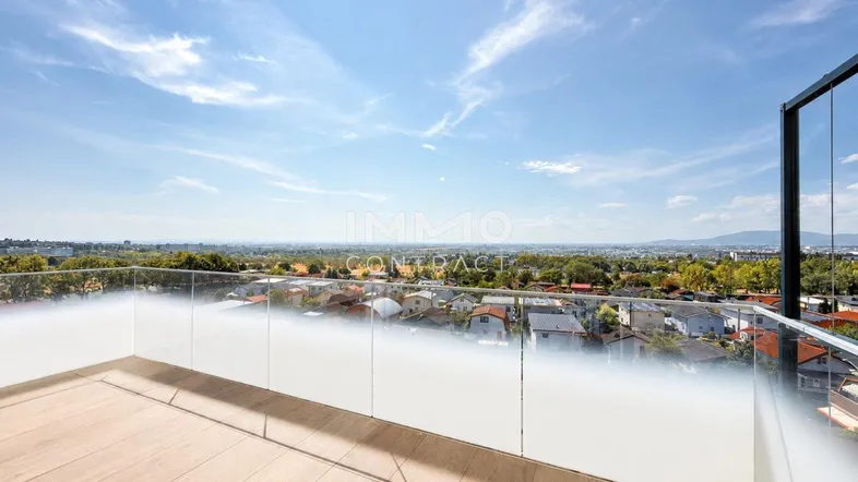 Geräumiger Balkon mit Glasgeländer und weitem Blick über die Stadt und die umliegende Landschaft.