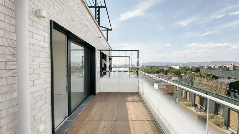 Geräumiger Balkon mit Holzboden, Glasgeländer und weitem Blick über die Stadt.