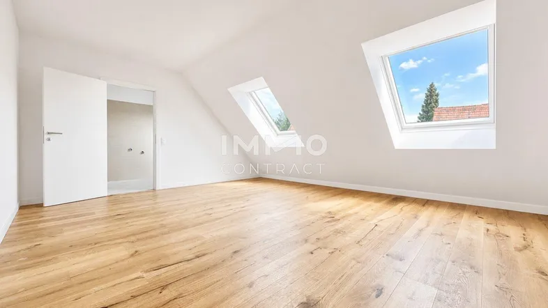 Helles Dachzimmer mit Holzboden, schrägen Wänden und zwei Dachfenstern, die viel Tageslicht hereinlassen.