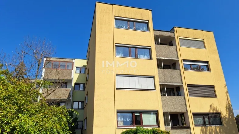 Gelbe Fassade eines Mehrfamilienhauses mit Balkonen unter blauem Himmel.