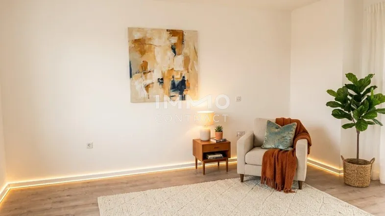 Helles Wohnzimmer mit moderner indirekter Beleuchtung, einem Sessel und einem dekorativen Wandbild.