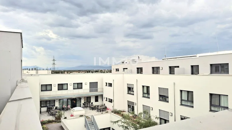 Blick von oben auf den Innenhof eines modernen Wohnkomplexes mit Sitzgelegenheiten.
