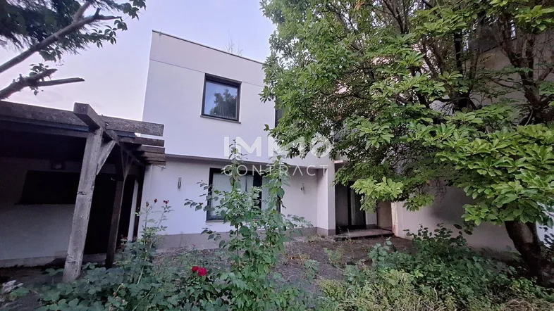 Rückansicht des Hauses mit verwildertem Garten und einer Holzpergola.