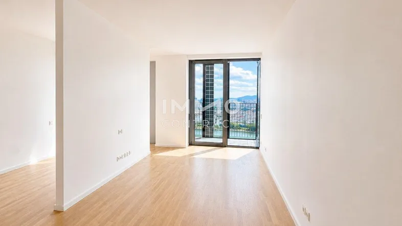 Helles, leeres Zimmer mit Holzboden und großen Fenstern, die einen weiten Blick auf die Stadt und das Wasser bieten.